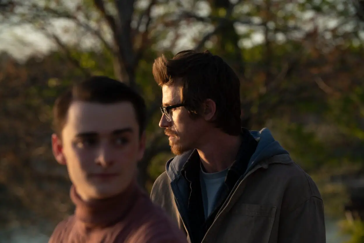Ethan (Garrett Hedlund) and Jackson (Noah Schnapp) stand in opposite directions in the forest, staring mysteriously into the distance.