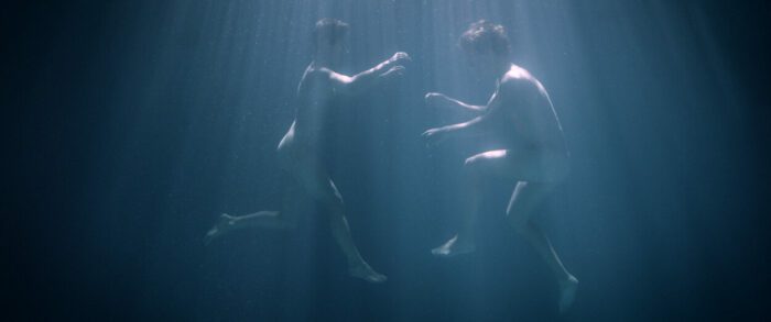 A man and woman float nude underwater.