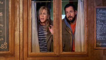 Jennifer Aniston as Audrey Spitz and Adam Sandler as Nick Spitz in peer through a restaurant door window.