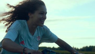 A young woman rides a motorbike, smiling as her hair blows in the wind.