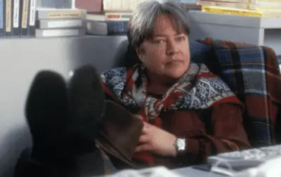 Kathy Bates sits with her feet on a desk in Primary Colors