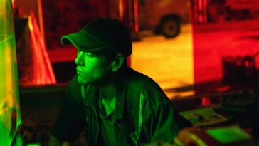 A Chinese Man wearing a baseball cap, in an image filtered in bright green, red, and yellow.