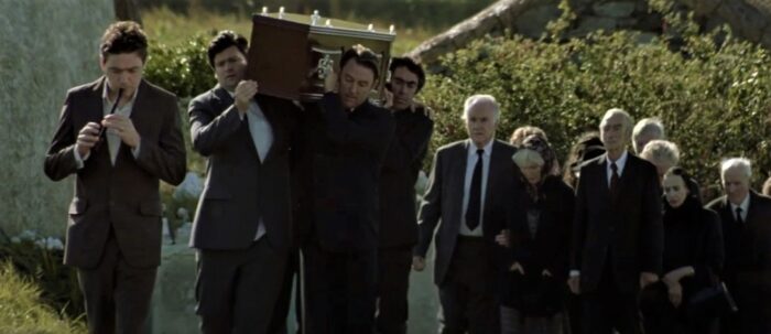 Funeral procession in the 1998 comedy film Waking Ned Devine featuring the town following a casket carried by some men.