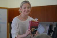 Kate Hudson as Prof. Cleary holds up a copy of the novel Goat Time.