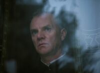 Malcolm McDowell as Timofeyev, looking through a windowpane.
