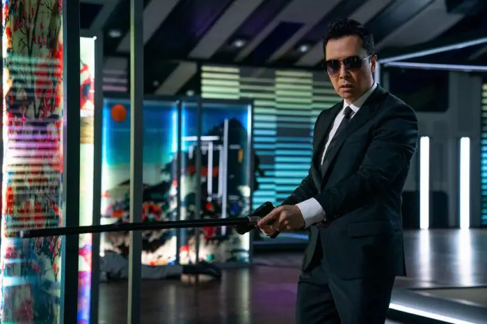 Donnie Yen in dark suit and sunglasses prowling a trophy room full of Japanese art as the blind assassin Caine in John Wick: Chapter 4