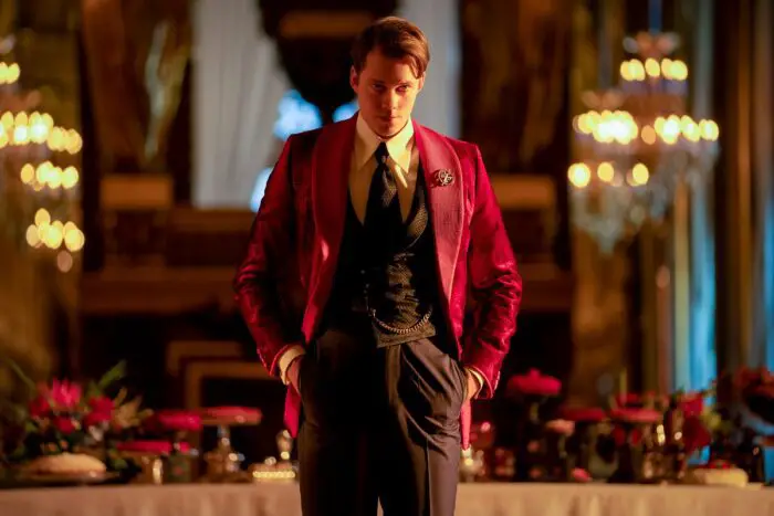 Bill Skarsgård in a red smoking jacket and black waistcoat, portraying the odious Marquis, an opulent, ruthless aristocrat in John Wick: Chapter 4.