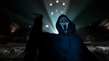 Ghostface raises their knife with lights illuminating them in the background.