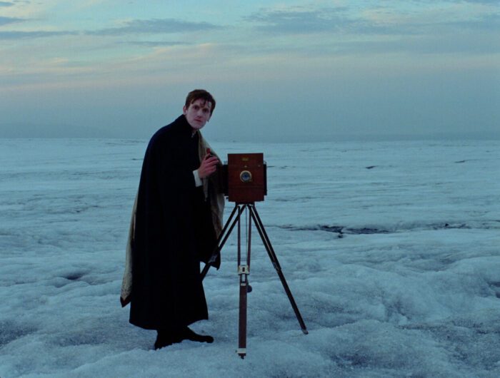 Lucas (Elliott Crosset Hove) surveys the snowy landscape with his camera in Godland.