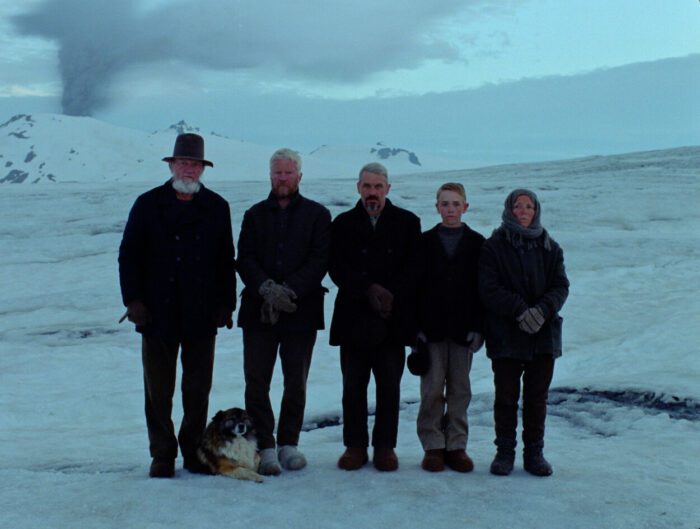 A group of characters pose for a photograph against the snowy Icelandic landscape in Godland.