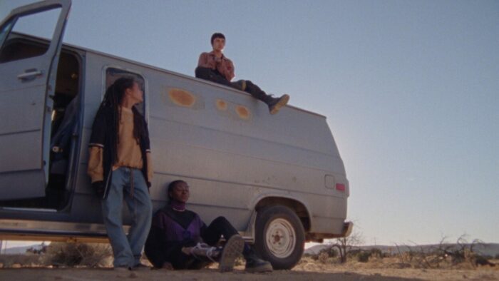 Theo (Sasha Lane) stands by the open door of a van in the Texan oilfields, beside her sits a wounded Alisha (Jayme Lawson) and on the roof Xochitl (Ariela Barer) is perched