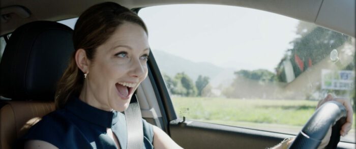 A woman cheers while driving a car.