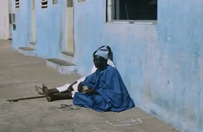 Screenshot of Xala showing a man dressed in blue sitting by a wall playing an instrument. 