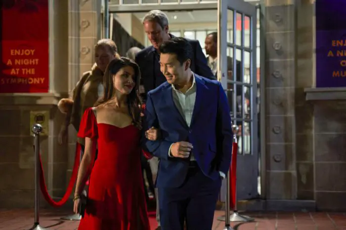 A man in a suit jacked leads a woman in a red dress outside.