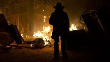 A shadowy figure stands in the middle of a town on fire