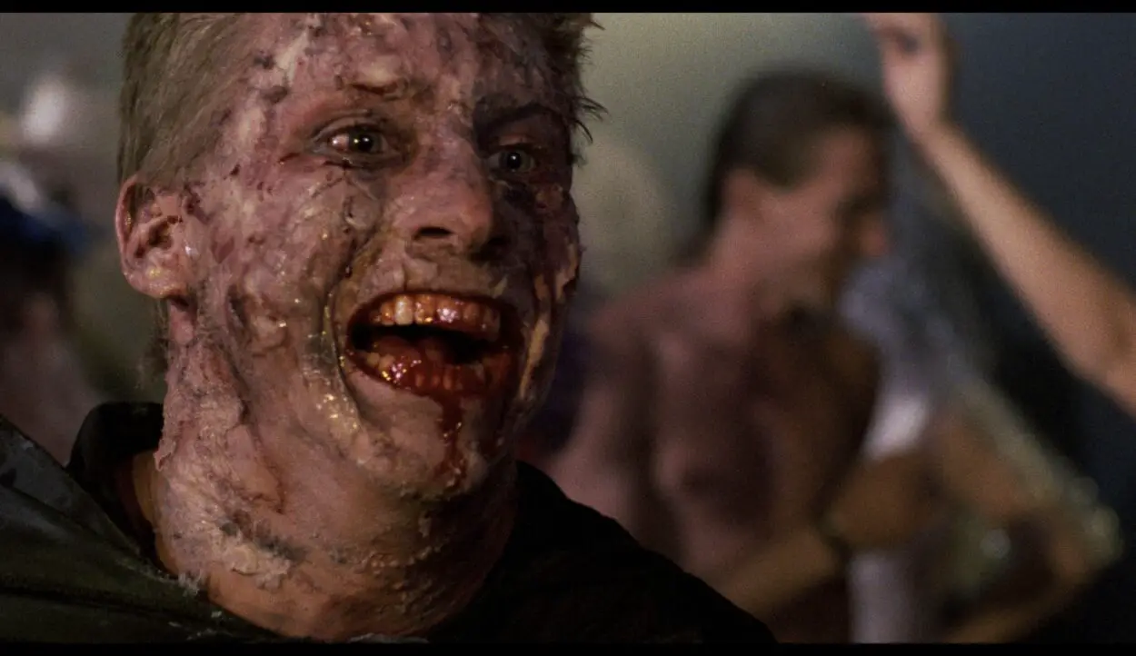 An infected man smiles with blood in his mouth and his skin discolored. 