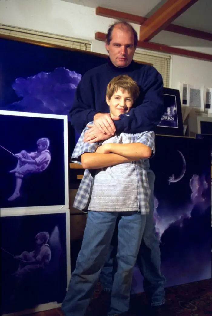 Robert Hunt wraps his arms around his son William as they both stand in front of paintings of the DreamWorks logo.