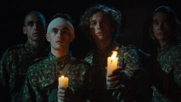Four young soldiers in combat fatigues hold up candles in the darkness.