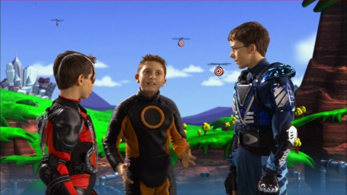 Arnold (Ryan Pinkston), Juni (Daryl Sabara), and Francis (Bobby Edner) talk inside the Level One of the video game. Floating bullseyes fly around their heads as they stand in a grassy area.