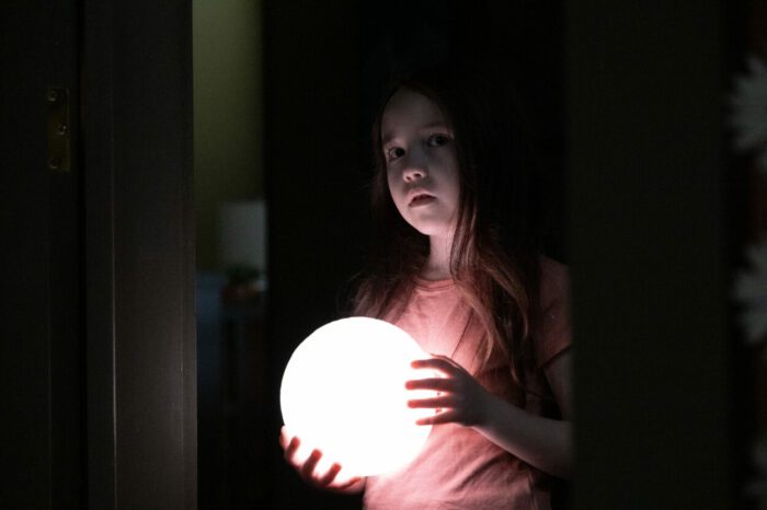 Vivien Lyra Blair as Sawyer Harper, surrounded by shadows and holding a small glowing model moon, in 20th Century Studios' THE BOOGEYMAN. Photo by Patti Perret. © 2023 20th Century Studios. All Rights Reserved.