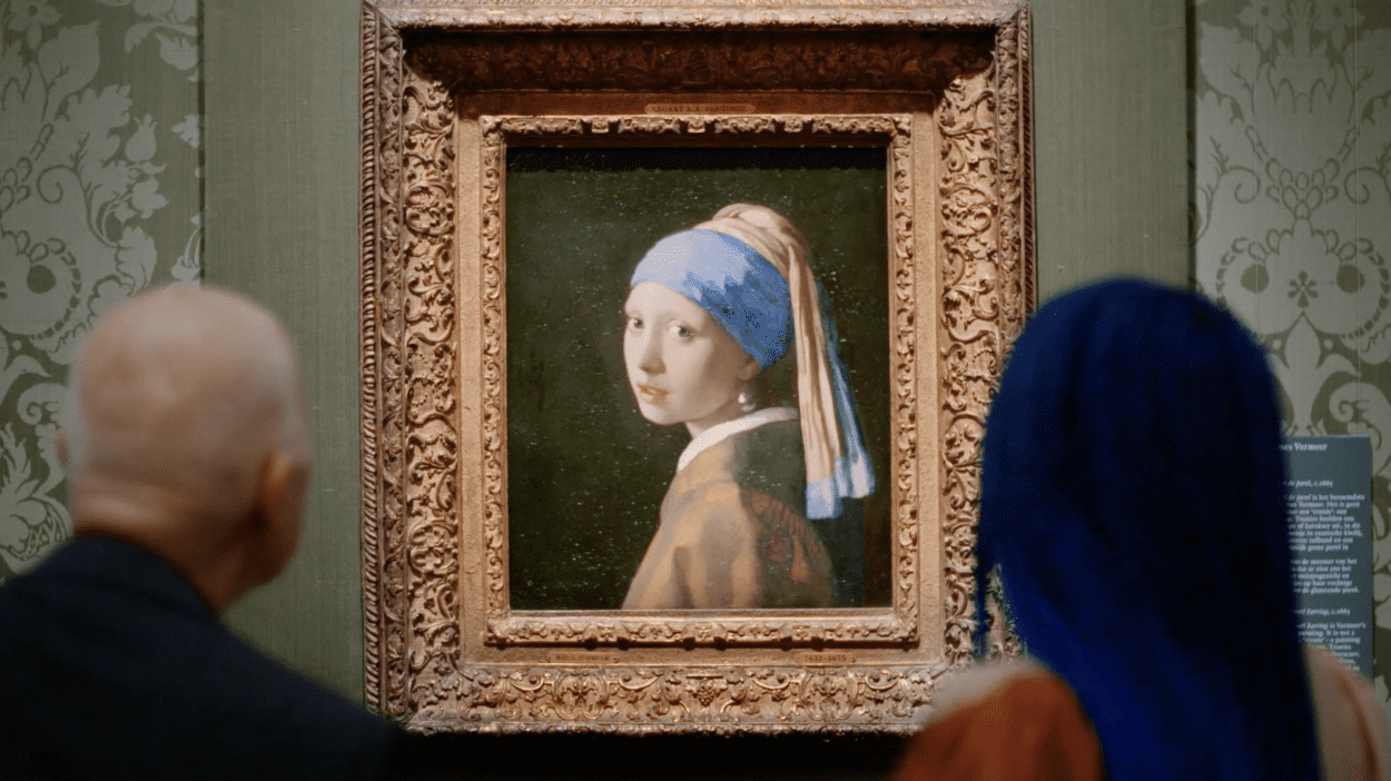 Man and a woman seen from the backs of their heads looking at Vermeer's The Girl with the Pearl Earring