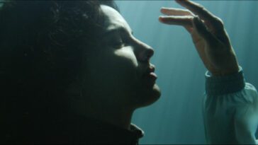 A woman looking serenely at her palm underwater.