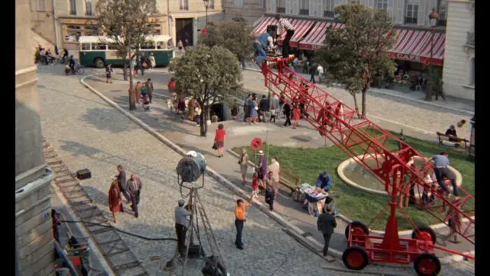 A busy overhead shot of a film set in a Parisian square with a crane and other equipment visible.