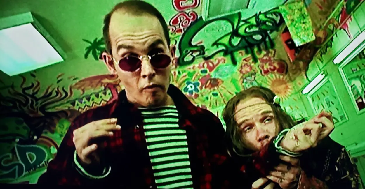 Flea and Johnny Depp as Raoul Duke and the hippie licking LSD off his sleeve in Fear and Loathing in Las Vegas (1998).