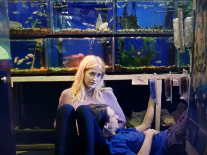 Gus Birney and Owen Campbell as Marlene and Drew sharing a tender moment amidst aquariums in a pet store in Giving Birth to a Butterfly (2021)