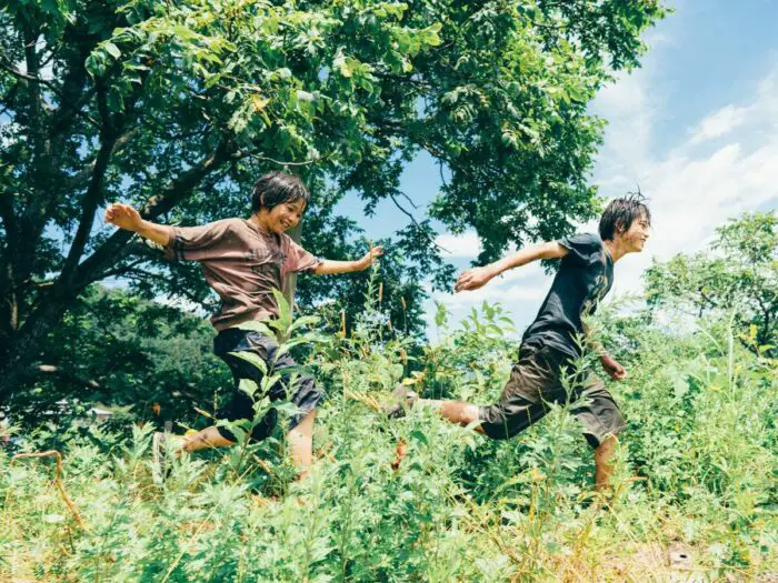 Two Asian youth run through a forest.