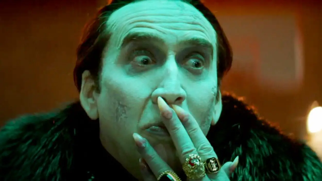A close up of Nicholas Cage gesturing as a green-tinted Dracula in Renfield.