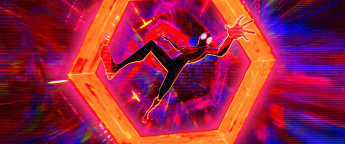 Miles Morales (Shameik Moore) travels the multiverse through a hexagonal shaped, orange colored portal surrounded by blue and purple lights.