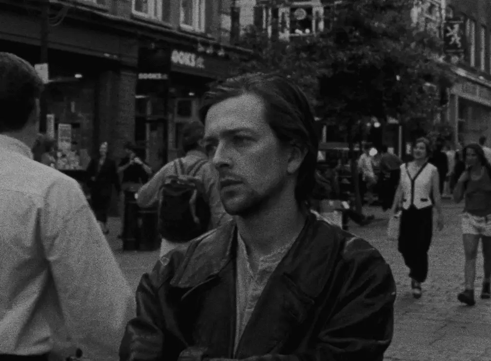 Screenshot from the movie Following. Shows a man with a sad look on a busy city street. 
