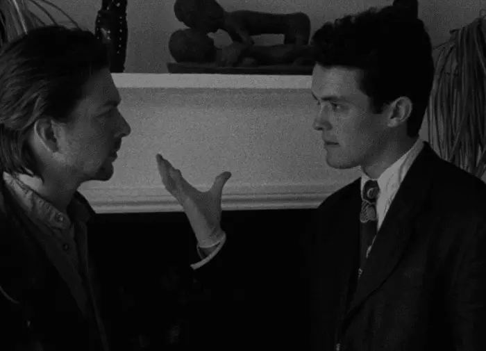 Screenshot from the movie Following showing two men in an apartment. The man on the right has his hand out.