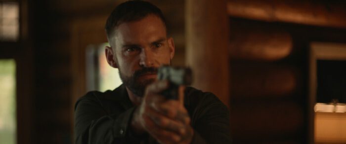 A bearded man points a gun off screen in The Wrath of Becky.