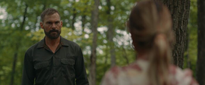 A bearded man confronts a teenage girl in the woods in The Wrath of Becky