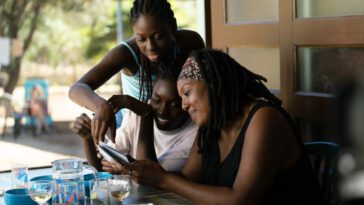 A mother (Aisattou Diallo Sagna) and her two daughters (Ester Gohourou and Suzy Bemba) gather at a dinner table to look at old photos
