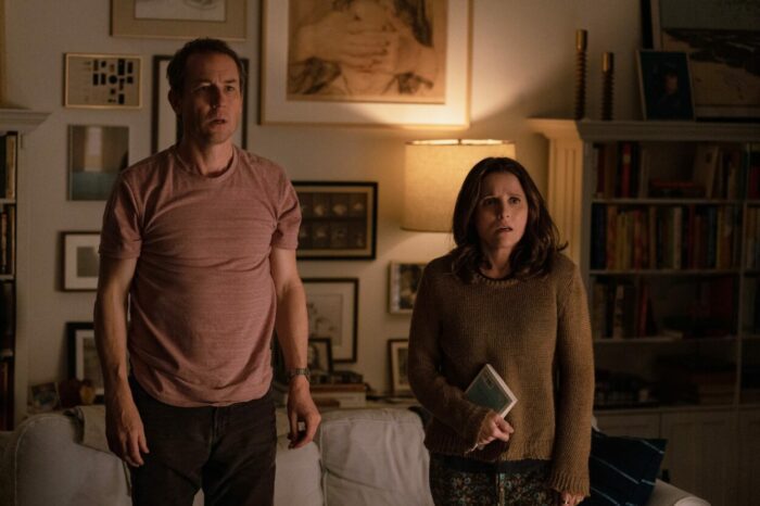 Don (Tobias Menzies) and Beth (Julia Louis-Dreyfus), standing up in their New York City apartment adorned with photos and paintings on the wall, look shocked and horrified at something.