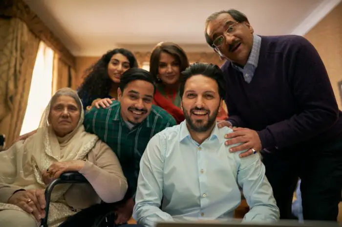 A man sits in front of his laptop camera backed by his extended family.