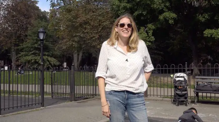 Blair Koenig stands and smiles in a park, wearing sunglasses and a loose white blouse and jeans.