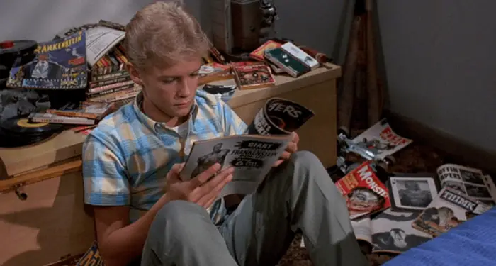 A teenage boy sits in his bedroom reading a magazine about monster movies