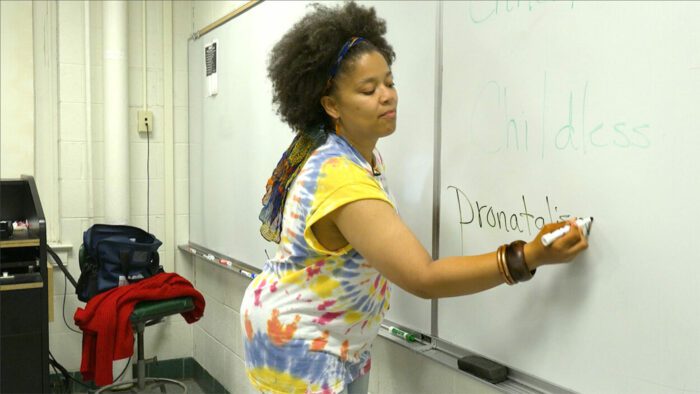 Kimya Dennis in the classroom, writing the word "Pronatalism" on the whiteboard.