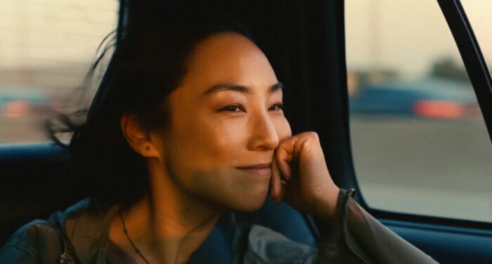 Greta Lee in Past Lives, smiling wistfully in a car window.