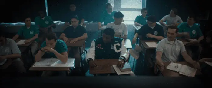 Three young men sit next to each other in a row of desks.