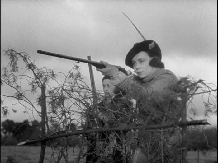 Image from The Rules of the Game: A woman dressed for a hunt aims a rifle.