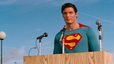 Superman stands at a podium of microphones