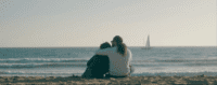 Javier and Cassandra sit on the beach, holding each other