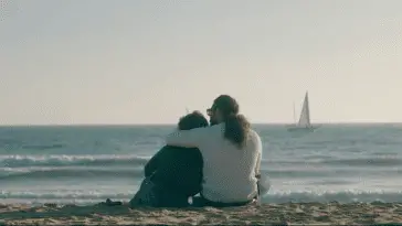 Javier and Cassandra sit on the beach, holding each other