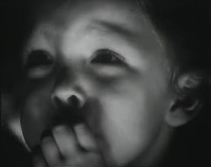 A young boy sticks his fingers in his mouth.