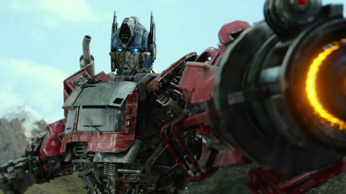 Optimus Prime aiming his gun to the center-right with some mountains in the background.